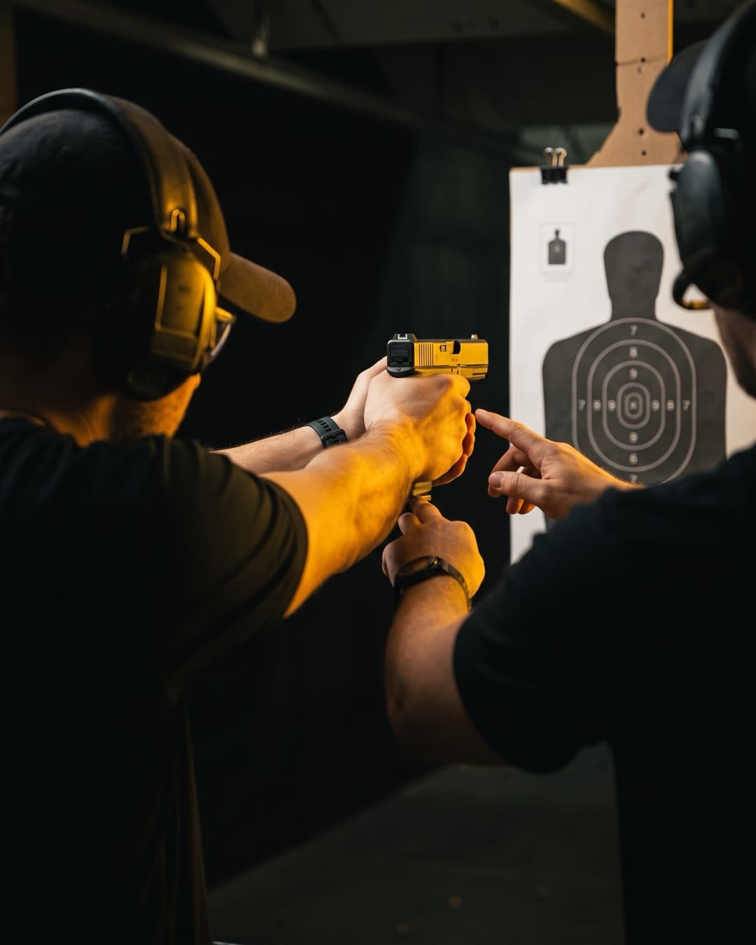Střelec s pistolí Glock míří na papírový terč, instruktor mu upravuje postoj